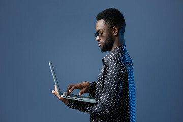 young african american man focused on using a laptop against a vibrant blue background, representing