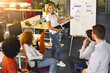 © Prostock-studio - A woman is standing in front of a whiteboard, delivering a presentation to an audience. She gestures and speaks confidently, engaging the viewers with her content.