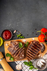 Wall Mural - Grilled beef steak on wooden cutting board with ketchup sauce and condiments, top view copy space