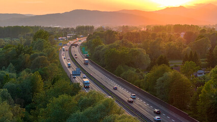 Wall Mural - AERIAL, LENS FLARE: Evening traffic on highway surrounded by trees and mountains