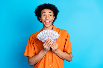 Poster - Photo of handsome good mood guy wear orange shirt spectacles holding cash fan emtpy space isolated blue color background