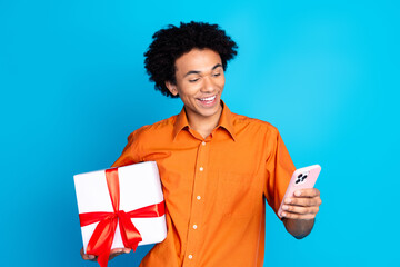 Poster - Photo of cheerful positive guy dressed orange shirt holding present box chatting device isolated blue color background