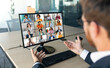 © Prostock-studio - A businessman sits at a desk in his office, with a computer screen displaying a video conference call with several other people. He is gesturing with his right hand