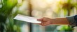 © Naret - Close-up of a hand holding an envelope in a green blurred background, symbolizing communication, delivery, or receiving a message.