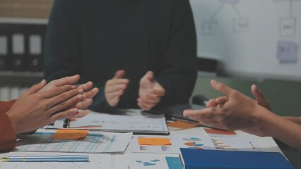A group of cheerful Asian graphic designers or developers is standing in the meeting, clapping their hands, and celebrating their successful project in the meeting together.