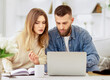 © Prostock-studio - A man and a woman are sitting together, looking attentively at a laptop screen in a room.
