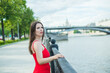 © SergeiPh - A woman in a red dress stands on a bridge overlooking a pond. She looks into the distance, perhaps lost in thought. Loneliness and contemplation concept