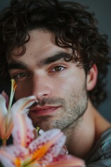 Wall Mural -  A man with curly hair holds a flower before his face, gazing seriously into the camera