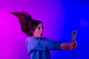 Poster - Photo of cheerful shcoked little lady dressed hoodie watching video modern gadget empty space isolated neon purple color background