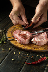 Wall Mural - Preparing a steak from meat by the hands of a chef for a barbecue. Raw meat on a kitchen cutting board with spices and pepper. Advertising space