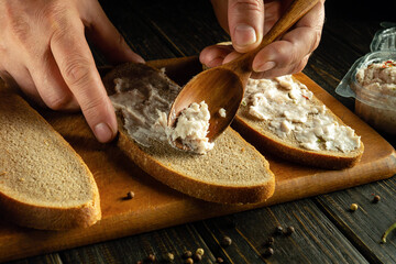 Wall Mural - Making sandwiches for a snack. The cook hand spreads grated fat with spices on bread with a spoon.