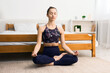 © Prostock-studio - Healthy lifestyle. Young woman exercicing in lotus position, sitting on floor in bedroom, free space