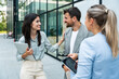 © Srdjan - Group of young successful business people, businessman and businesswoman standing out of office building in formal wear, discussing about business. Cool happy expatriate company experts exchange info