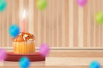 Birthday cupcake with burning candle on wooden background with colorful balloons