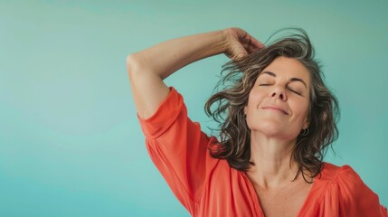 Wall Mural - A woman with closed eyes smiling and touching her hair wearing an orange blouse against a blue background.