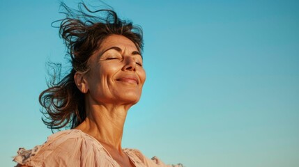 Wall Mural - A woman with closed eyes smiling and her hair blowing in the wind against a clear blue sky.