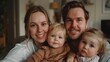 © iuricazac - A family of four with a man and woman smiling at the camera holding two young children one in each arm in a cozy indoor setting.