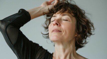 Wall Mural - Woman with closed eyes hand on head in black top against white background with relaxed facial expression.