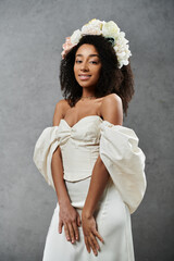 Wall Mural - A beautiful African American bride in a white wedding dress and a floral crown smiles against a grey backdrop.