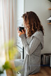 © ASTA Concept - Young pretty woman drinks coffee sitting at her kitchen at home and looking out the window enjoys of morning.