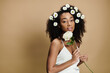 © LIGHTFIELD STUDIOS - A beautiful African American woman with natural makeup and flowers in her hair poses against a beige background.