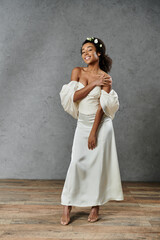 Wall Mural - An African American bride in white dress, flowers in hair, beaming with joy against grey backdrop.