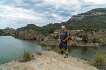 Wall Mural -  A strong man hiker poses smiling on a rock, with a landscape with mountains and a lake in the background