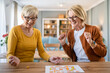 © Miljan Živković - two senior women friends or sisters play leisure board game at home