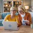 © Miljan Živković - Senior women two females hold credit card online shopping at home