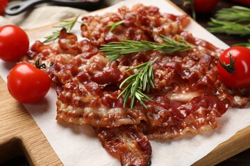 Slices of tasty fried bacon, rosemary and tomatoes on table, closeup