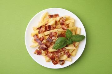 Wall Mural - Delicious French fries with slices of bacon and basil on green background, top view