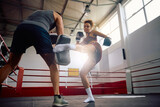 Female fighter practicing leg kick during sports training with her instructor in health club.