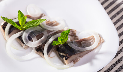 Sticker - Slices of pickled herring with onions decorated mint leaves served on white plate..