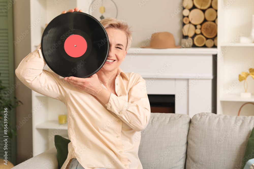 Mature woman with vinyl disk for record player sitting on sofa at home