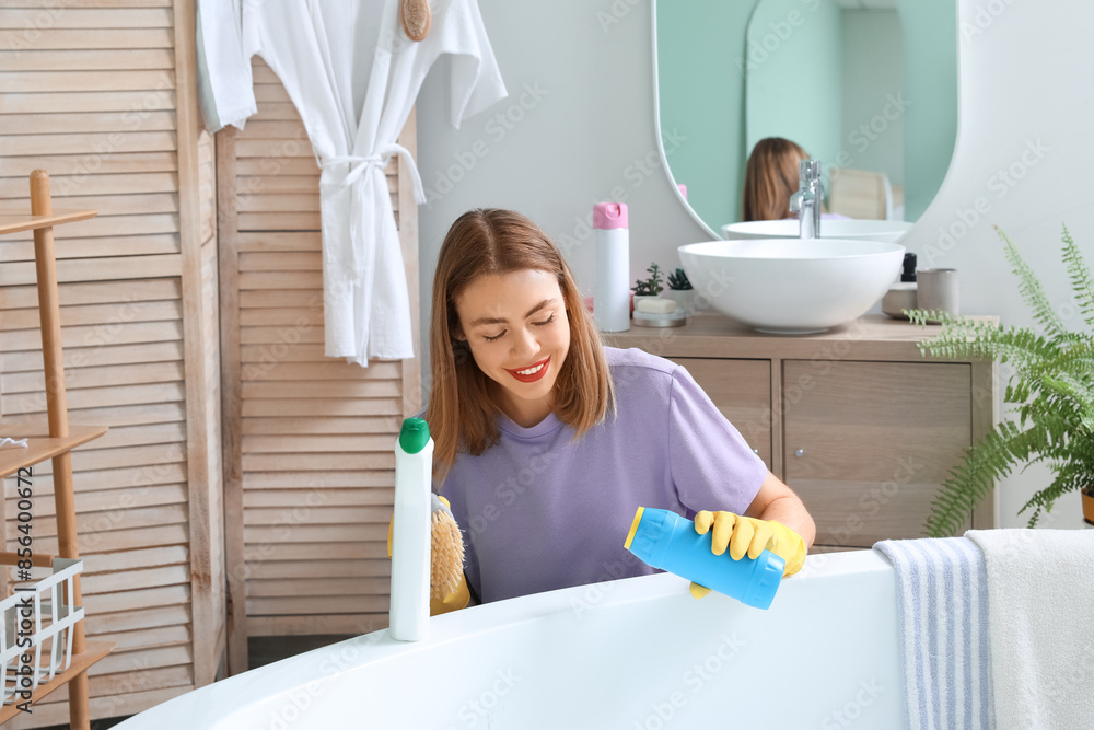 Young woman cleaning bathtub in bathroom