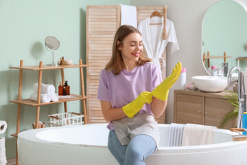 Poster - Young woman putting rubber gloves in bathroom