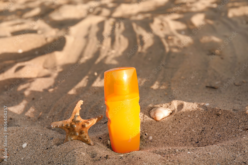 Bottle of sunscreen cream with starfish on sand at beach