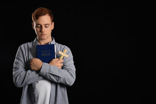 Young redhead man with Bible and wooden cross on black background