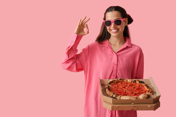 Poster - Beautiful young woman in sunglasses with tasty pizza showing OK gesture on pink background