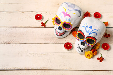Painted human skulls with burning candles and beautiful flowers for Mexico's Day of the Dead on white wooden table