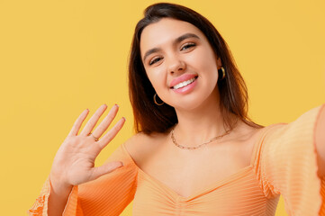 Canvas Print - Young woman waving hand on yellow background, closeup. Online dating concept