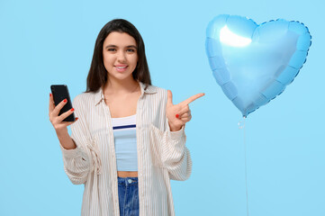 Canvas Print - Young woman with mobile phone pointing at balloon on blue background. Online dating concept