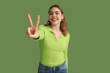 Wall Mural - Pretty young woman showing peace gesture on green background