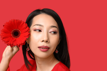 Wall Mural - Pretty young Asian woman with beautiful gerbera flower on red background