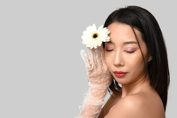 Poster - Pretty young Asian woman with white gerbera flower on grey background