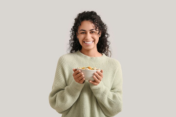Wall Mural - Happy young woman holding bowl of tasty cereal rings on light background