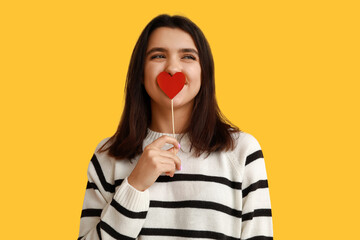 Wall Mural - Beautiful young girl with red paper heart on yellow background. Valentine's Day celebration