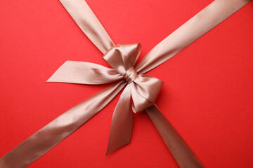 Wall Mural - Beige satin ribbon with bow on red background, closeup