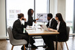 © sofiko14 - Business professionals discussing company strategy during office meeting. Woman presenting graphs on screen while colleagues listen attentively. Modern office with large windows and city view.