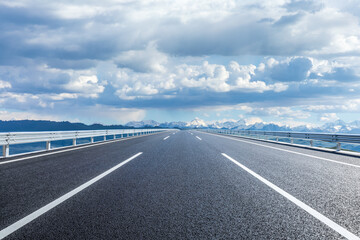 Wall Mural - Straight asphalt highway road and snow mountains with sky clouds natural landscape. car background.